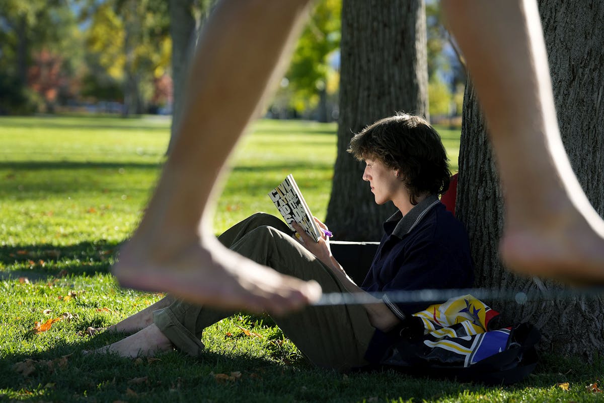 First-year student Logan Thompson reads a book on a warm October afternoon as others walk slack line on campus. Photo by Jamie Cotten / Colorado College